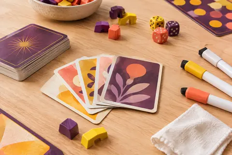 Cartes, supports colorés et crayons effaçables de Just One réunis sur une table de jeu en bois clair.
