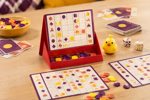 Jeu de mots mêlés junior rouge avec grilles et lentilles de couleur sur une table en bois clair.