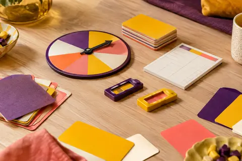 Cartes multicolores, cadran de score et révélateurs du jeu Password posés sur une table en bois clair.