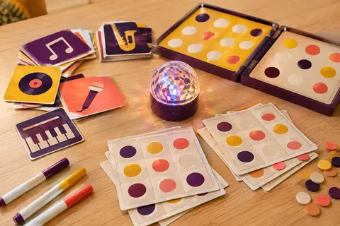 Boule disco, plateau de bingo musical, cartes et stylos disposés sur une table en bois clair