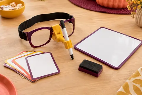 Porte-stylo à lunettes, tableau effaçable, marqueur, effaceur et cartes de jeu sur une table