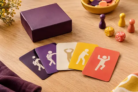 Boîte de jeu de mime au format poche et cartes multicolores posées sur une table en bois clair