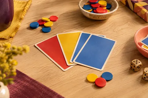 Cartes et jetons rouges, jaunes et bleus disposés sur une table en bois clair pour un jeu de bluff.