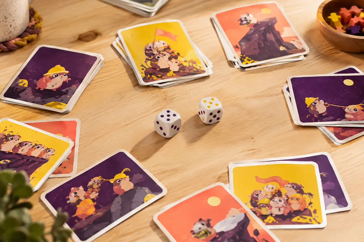 Cartes multicolores et deux dés de jeu disposés sur une table en bois clair.