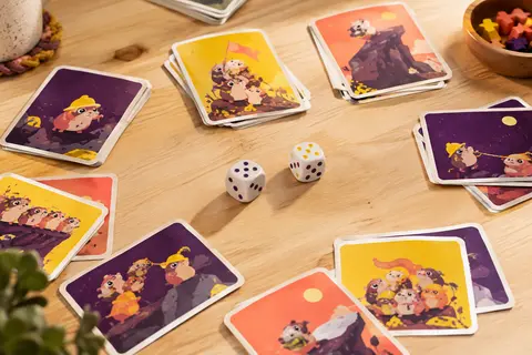 Cartes multicolores et deux dés de jeu disposés sur une table en bois clair.